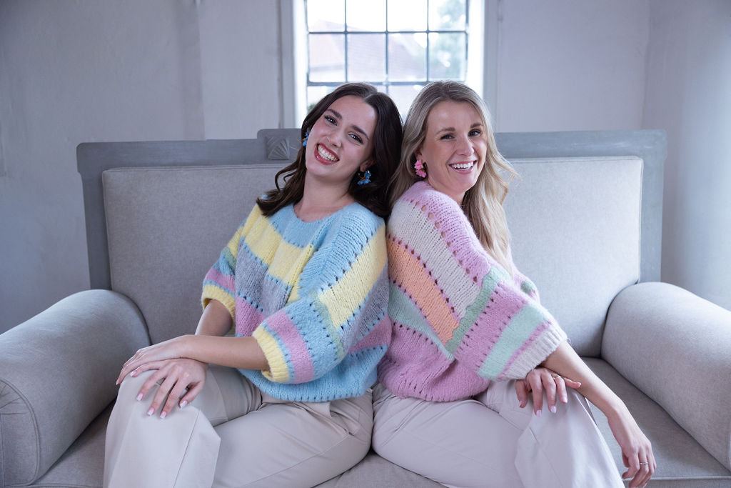 Lachende Freundinnen mit bunten Strickpullovern im Wohnzimmer