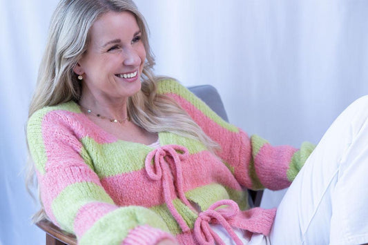 Frau lachend in pink-grünem Streifenpullover auf Stuhl
